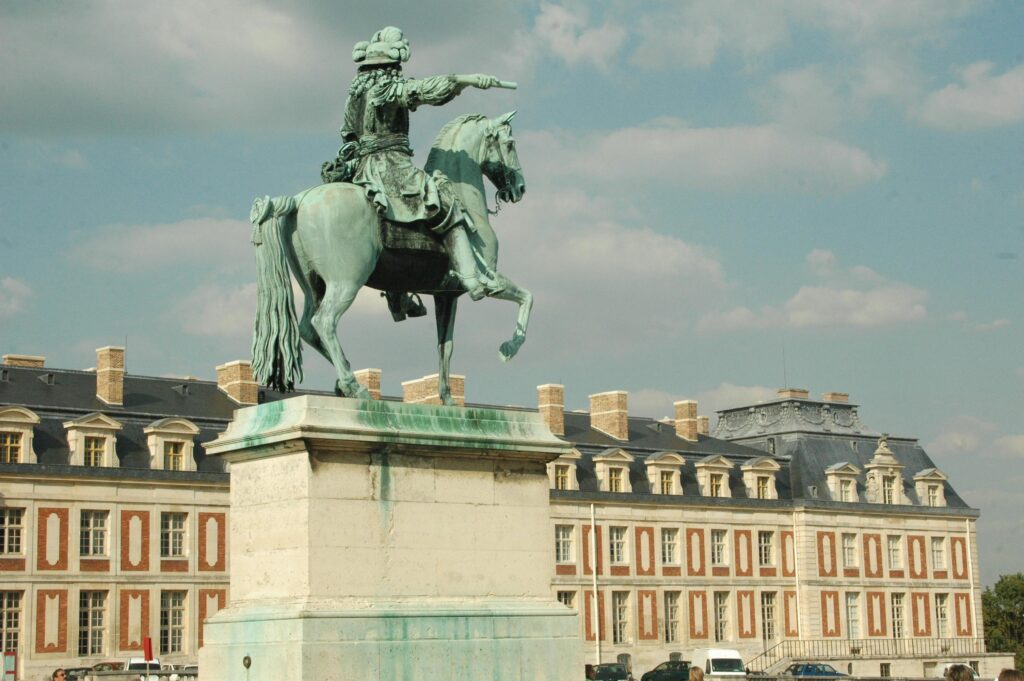 Historic equestrian statue of Louis XIV at the Palace of Versailles, France, under a blue sky.