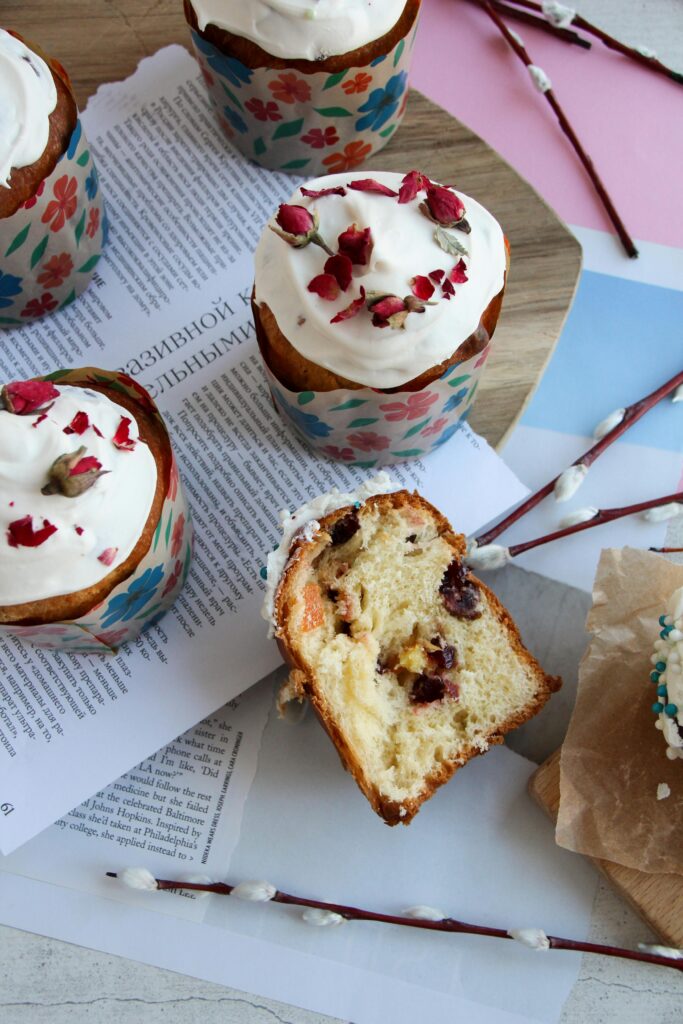 Colorful cupcakes with cream and berries, set on a rustic table with cyrillic text and willow twigs.